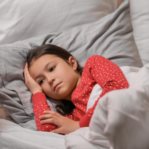 Young girl lying bed, she has dark hair and a red polka dot shirt